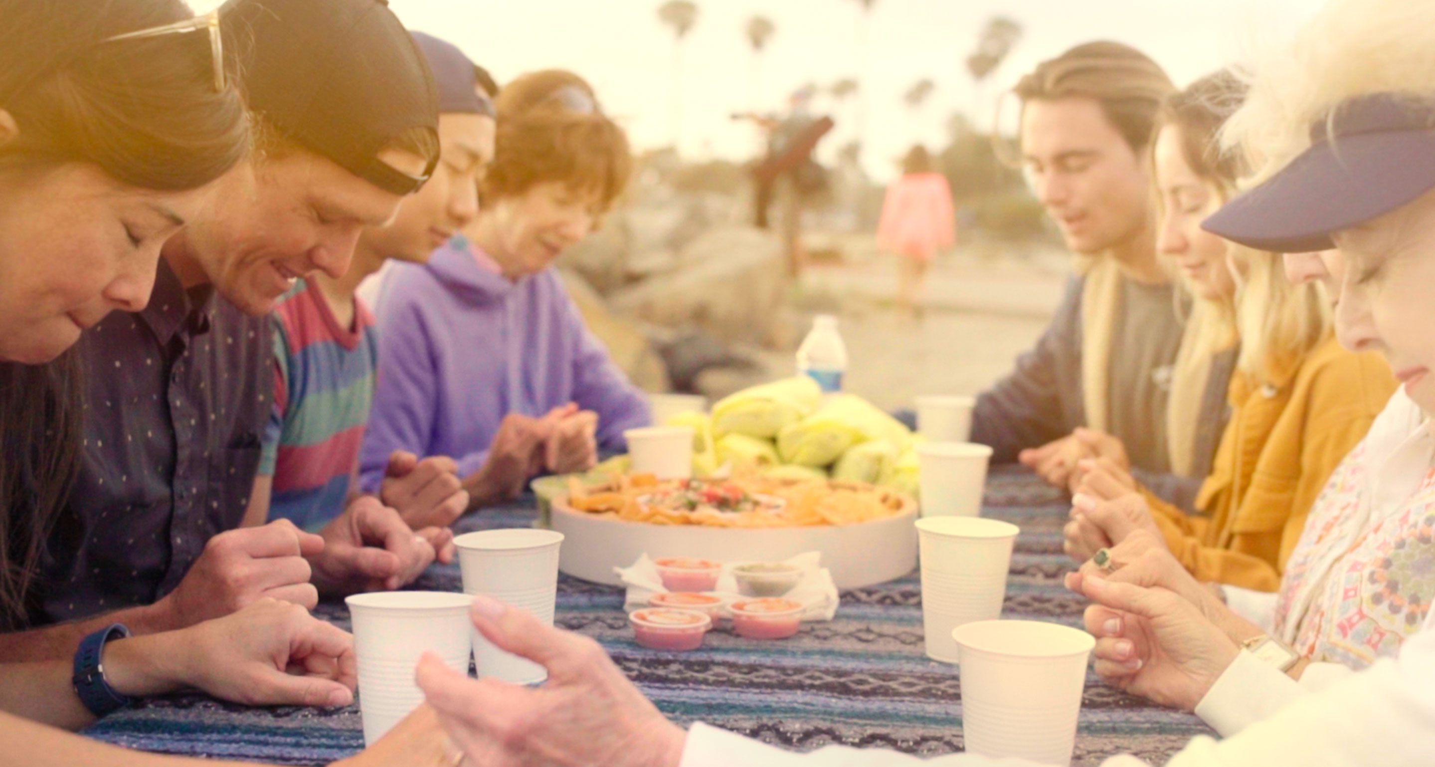 Group of people holding hands and praying at an outdoor picnic.